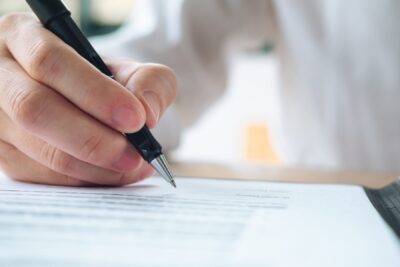 Person signing a legal document with a pen, illustrating the preparation of a car accident demand letter to the insurance company before the car accident settlement process begins.