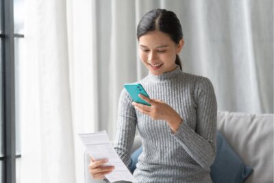 Employee reviewing a pay stub and her phone at home to confirm hourly pay matches the current state minimum wage
